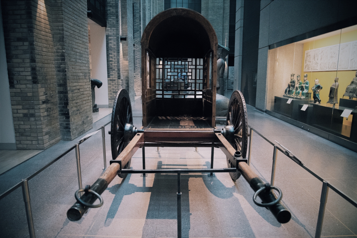 Wooden two-wheeled horse-drawn cart with a covered top displayed in a museum.
