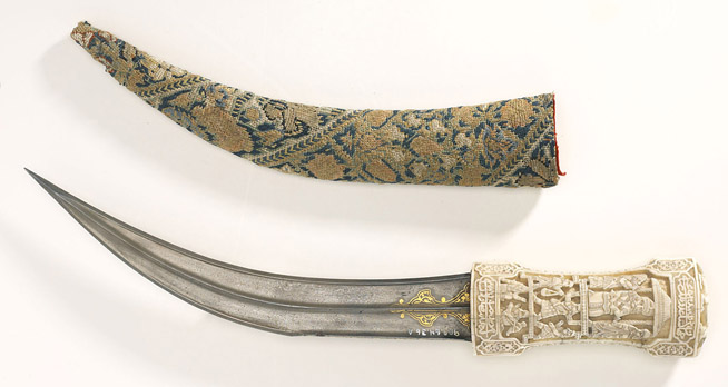 Curved dagger with an intricately carved ivory handle and a sheath decorated with a floral pattern.