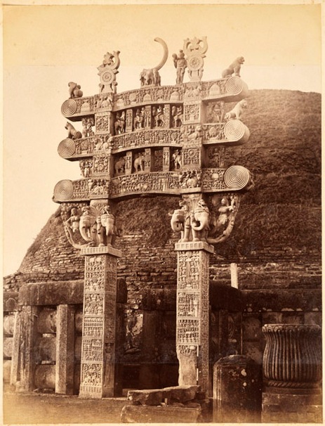 Wooden entrance structure with carvings of human and animal figures and decorated columns.
