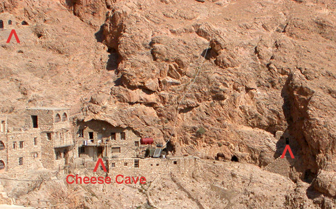 Cheese Cave carved into a rocky cliff with small stone buildings at its base.