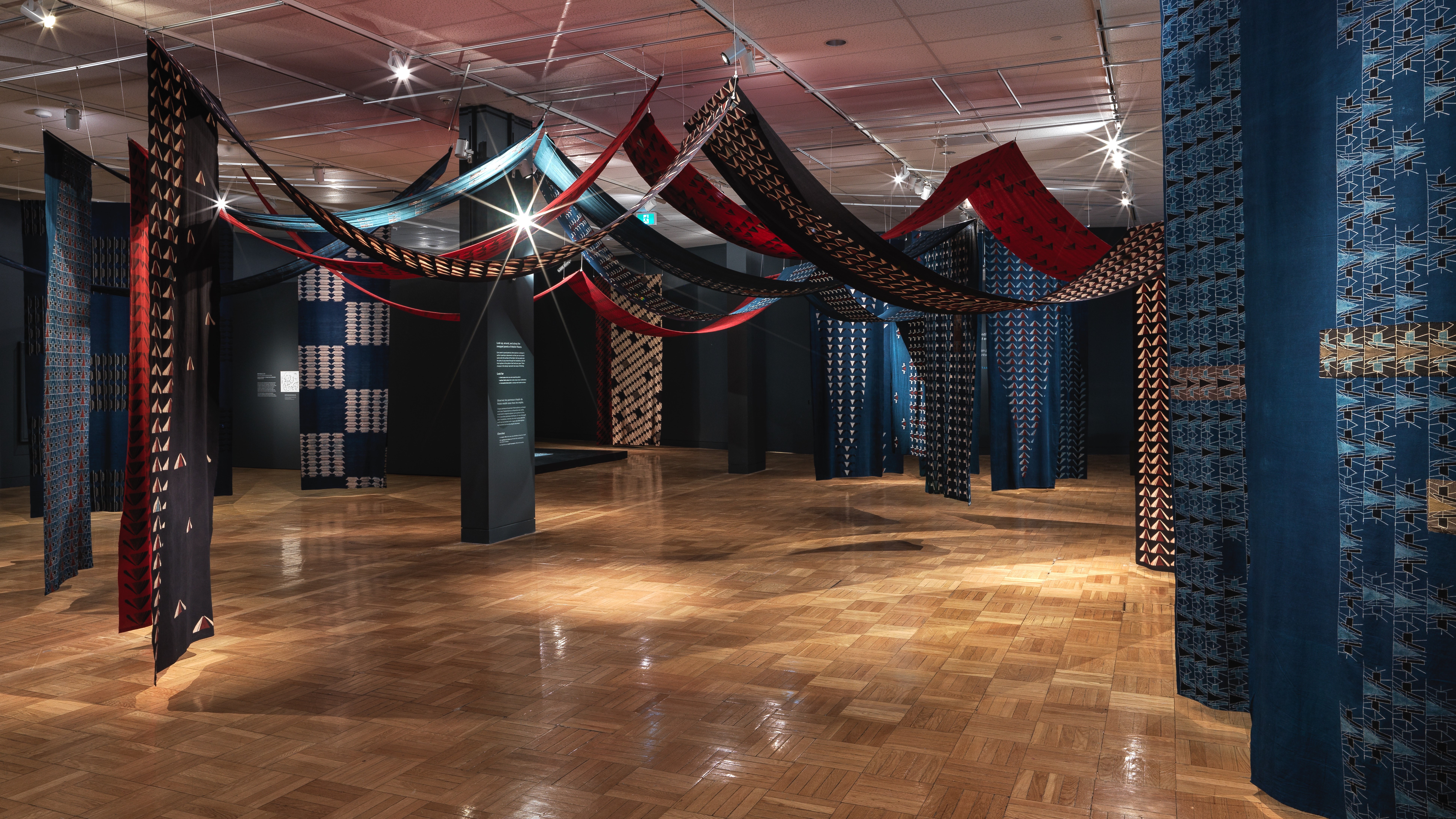 Vue panoramique d'une installation de sculpture souple composée de longueurs de tissu de coton imprimé suspendues en hauteur.