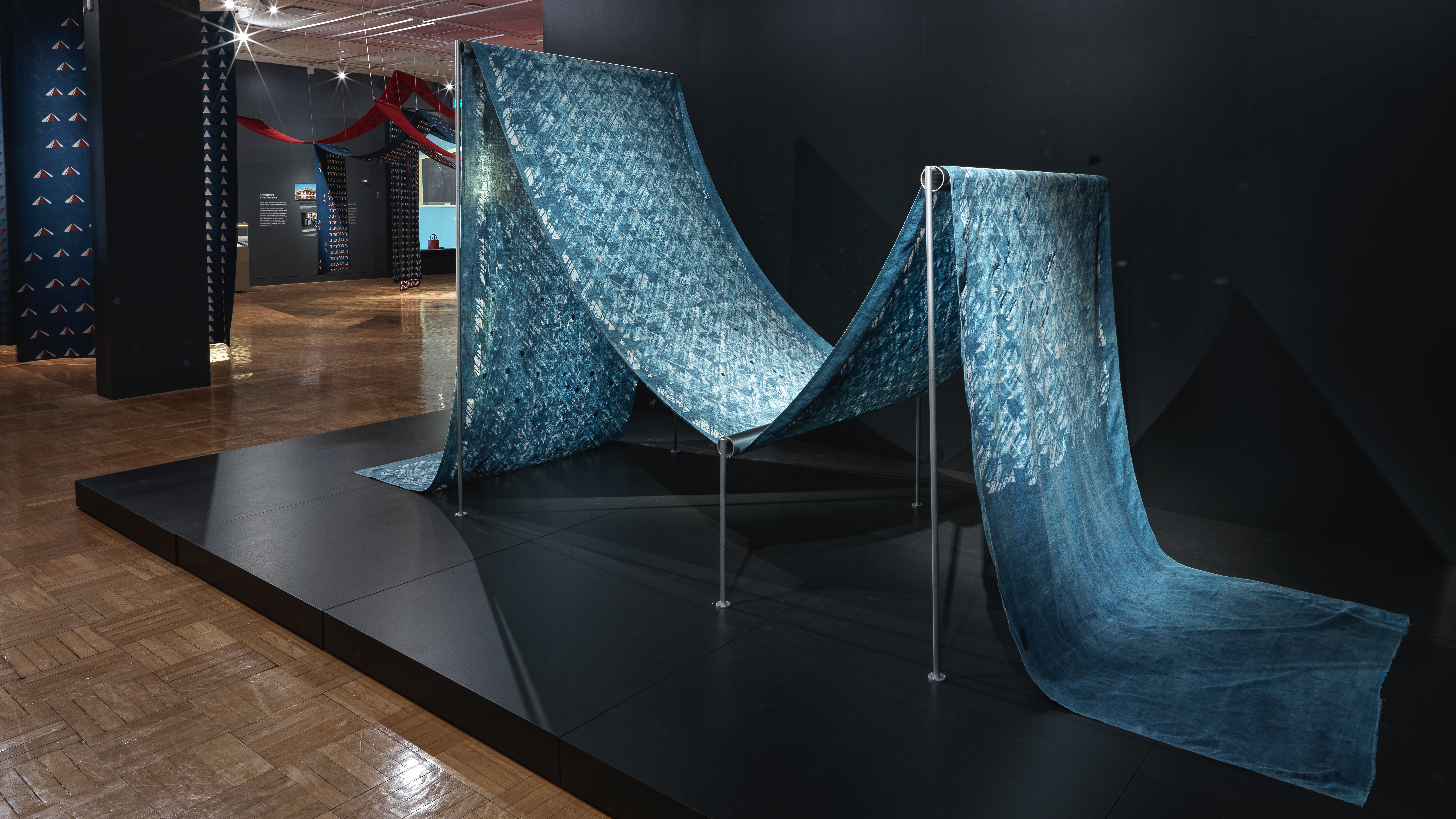 Vue d'une longueur de tissu de coton bleu teint avec des embellissements en miroir disposés sur un cadre pour ressembler à un tissu sur un métier à tisser dans l'exposition Swapnaa Tamhane : Mobile Palace, au ROM.