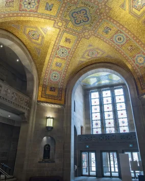 The ceiling of the ROM Rotunda the gold tiles shimmer in the light coming through the stain glass window.