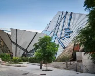 Modern angular building with reflective metal panels and a sculpture of a blue maple leaf on the facade.