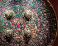 Ornate circular shield featuring intricate patterns with raised silver studs against a colorful floral background.