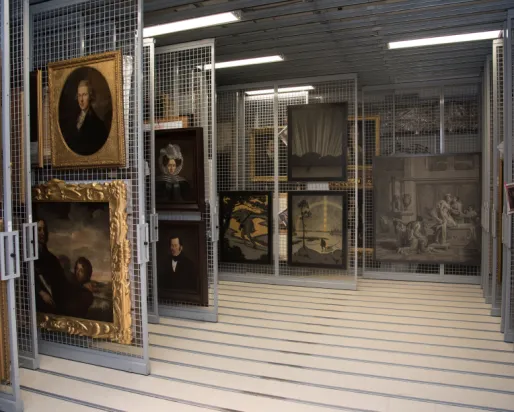 Gallery storage area showing hanging framed portraits and artworks in a well-lit room with striped floor.