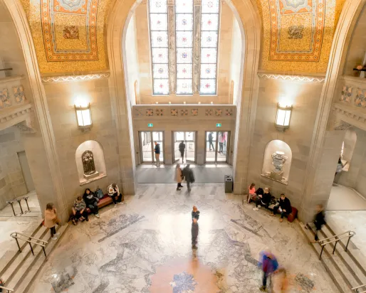 Spacious museum entrance hall with high arched ceiling, detailed wall carvings, and symmetrical seating areas along the sides.