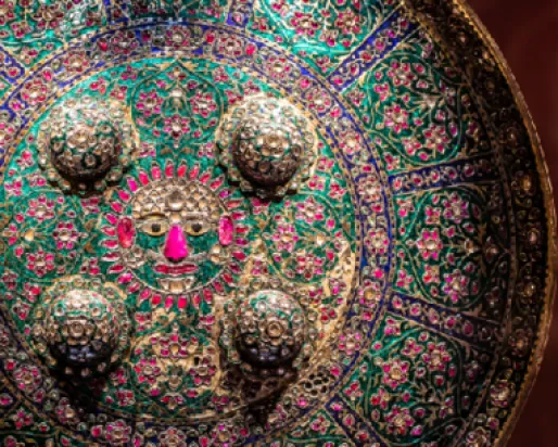 Ornate circular shield featuring intricate patterns with raised silver studs against a colorful floral background.