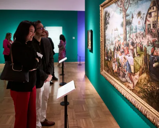 Two visitors closely observing a large framed painting displayed on a teal gallery wall.