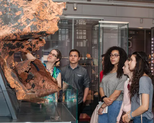 Diverse teenage students examine a twisted sheet of copper with guidance from a teacher
