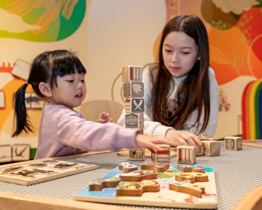 Two children playing with wooden blocks at a table inside a colorful room.