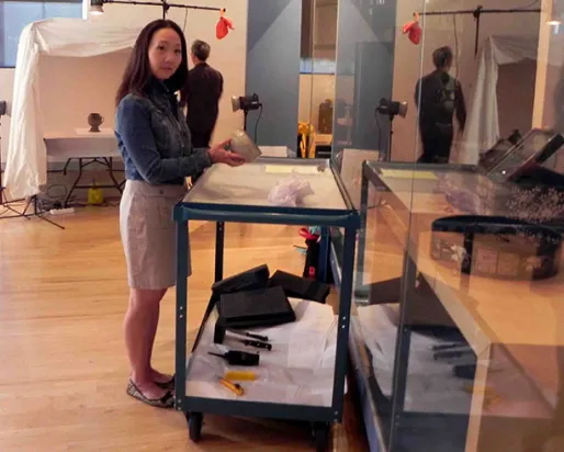 A woman standing next to a desk with a box on it inside a museum gallery space.