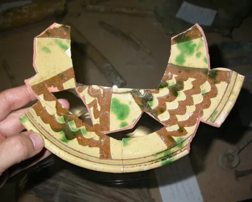 Pottery with an earthenware fired-clay body, overall white slip, incision through the slip with a broad tool, overall lead glaze, splashed with copper-green, probably mid-14th century.
