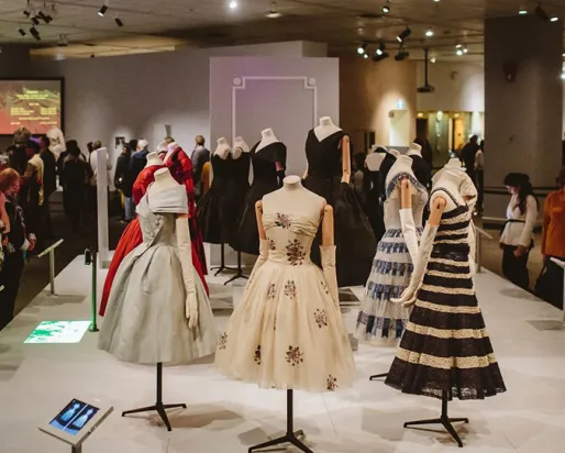 Dior dresses on display in museum space.
