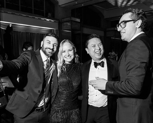 Five people in formal attire smiling and posing indoors at a social event.