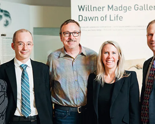 Five adults in business attire stand and smile in front of a sign reading “Willner Madge Gallery Dawn of Life.”
