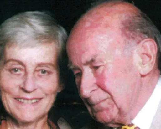 Portrait of an elderly woman with short gray hair smiling, beside an elderly bald man with a yellow tie and suit.