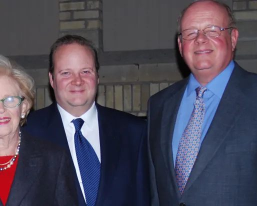 Three people posing closely together, all wearing formal attire against a neutral indoor background.