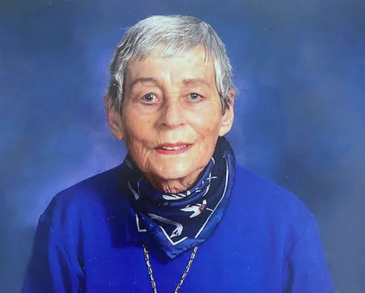 Portrait of an older woman with short gray hair, wearing a blue sweater and a patterned scarf.