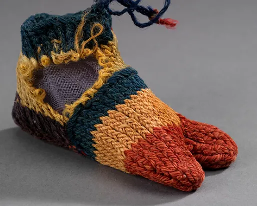 Woven baby shoes with orange toes, yellow and green bands, and blue laces on gray background.