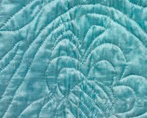 Close-up of a light blue fabric with stitched quilted patterns including a butterfly and symmetrical lines.