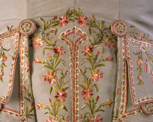 Gros plan sur un tissu beige brodé de motifs floraux roses et verts et décoré de perles.