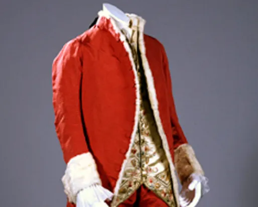 Red 18th-century coat with white lace cuffs and a patterned waistcoat underneath.