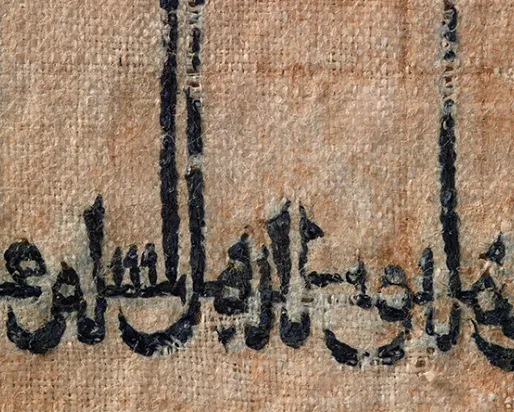 Arabic script in black ink on a tan, textured surface, possibly parchment or fabric.