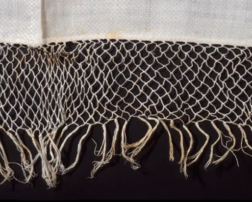 Close-up of beige woven net with knotted fringe on a black background.