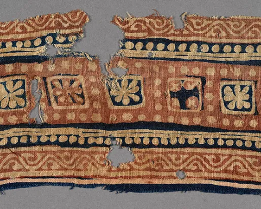 Decorative textile fragment with geometric and floral patterns in blue, beige, and red tones.