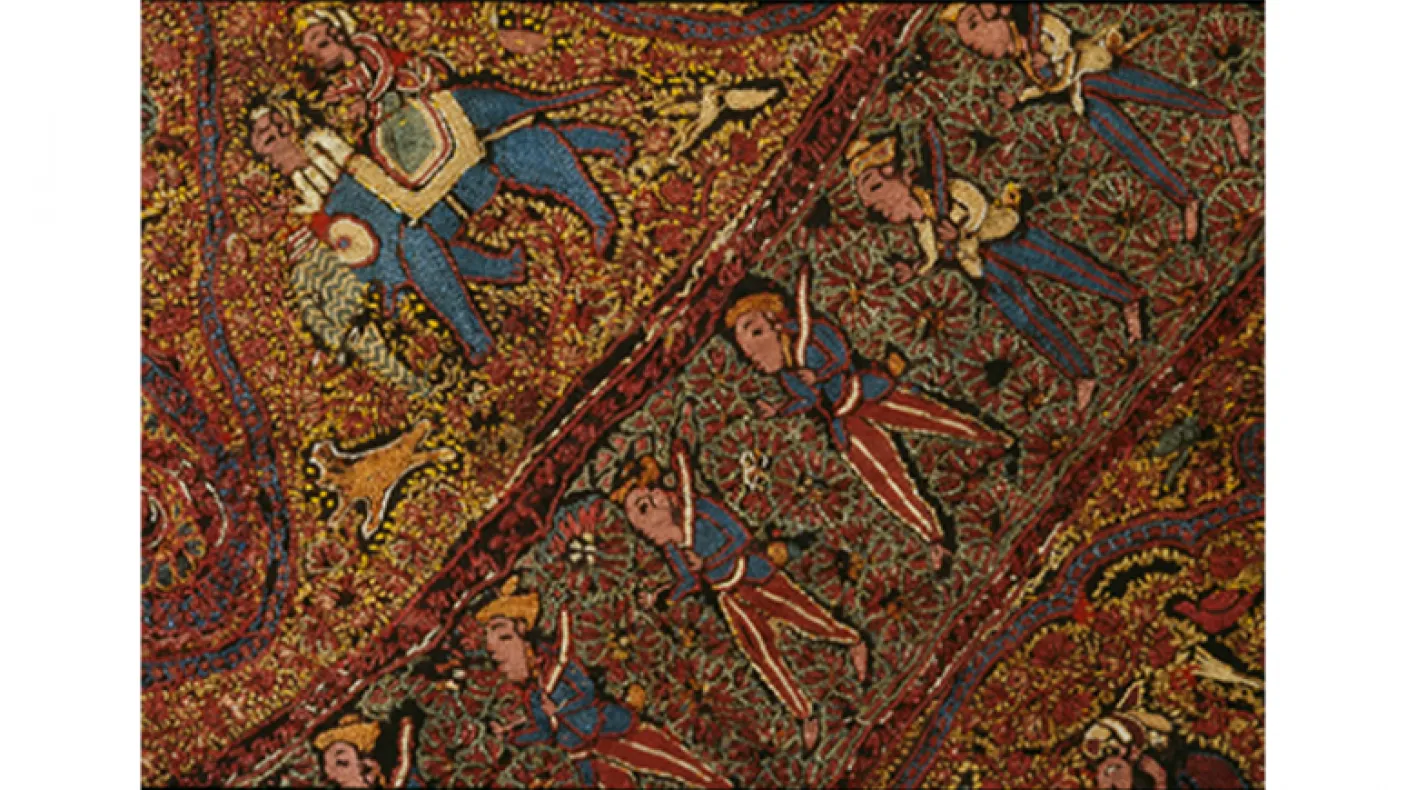 Colorful textile with intricate patterns depicting human figures, elephants, and floral motifs on a reddish-brown background.
