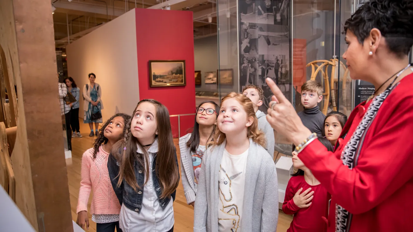 Un groupe d'enfants écoute un guide expliquer une exposition.