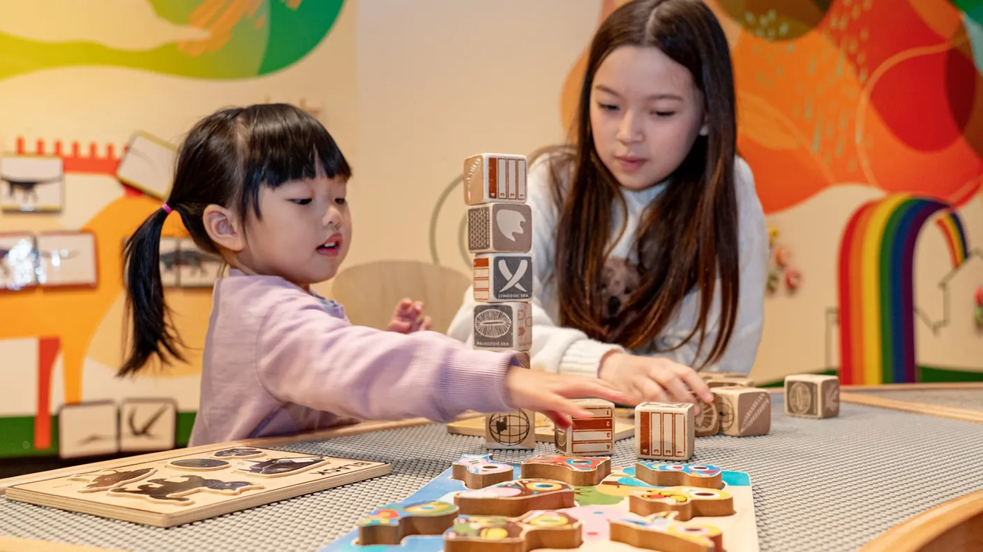 Two children playing with wooden blocks at a table inside a colorful room.