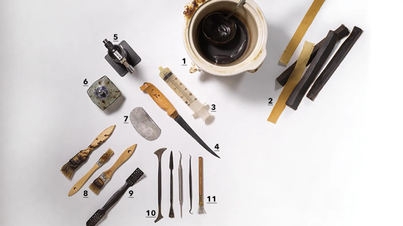 Divers outils traditionnels, dont des couteaux, des grattoirs et de petits objets sculptés, disposés sur une surface blanche à côté d'une tasse de café.