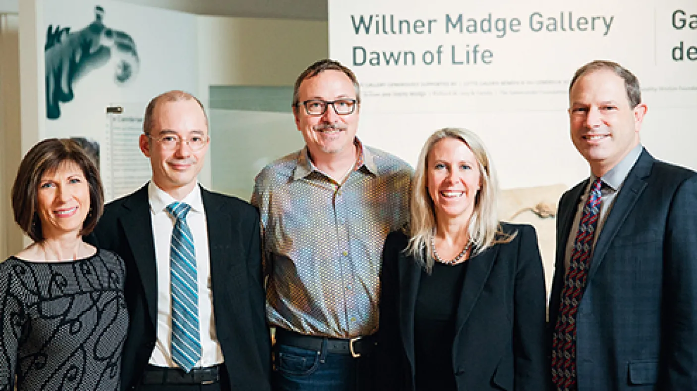 Five adults in business attire stand and smile in front of a sign reading “Willner Madge Gallery Dawn of Life.”