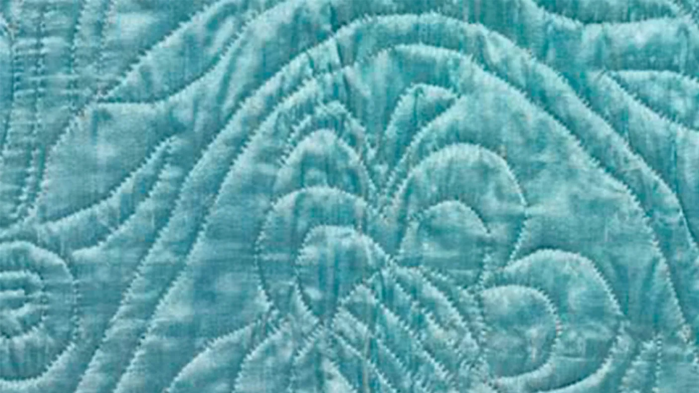 Close-up of a light blue fabric with stitched quilted patterns including a butterfly and symmetrical lines.