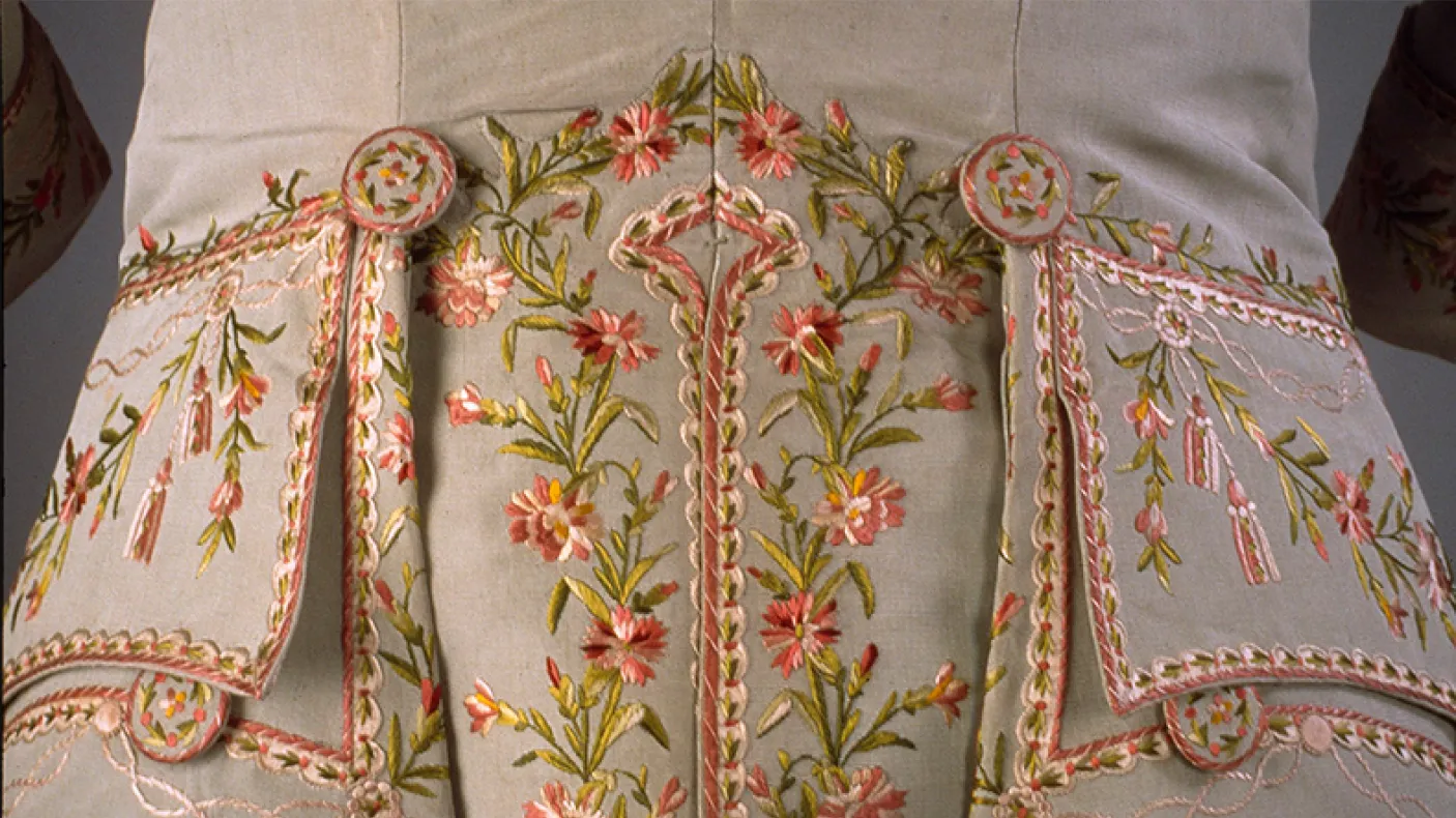 Gros plan sur un tissu beige brodé de motifs floraux roses et verts et décoré de perles.
