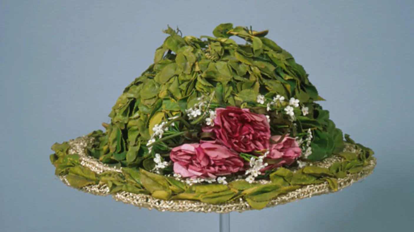 Green hat decorated with pink and white flowers and green leaves, with lace trim.