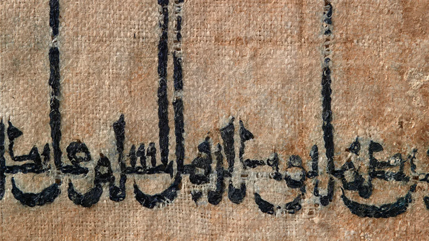 Écriture arabe à l'encre noire sur une surface havane et texturée, peut-être un parchemin ou un tissu.