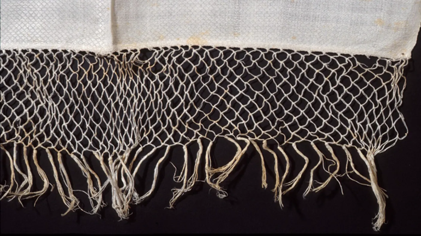 Close-up of beige woven net with knotted fringe on a black background.
