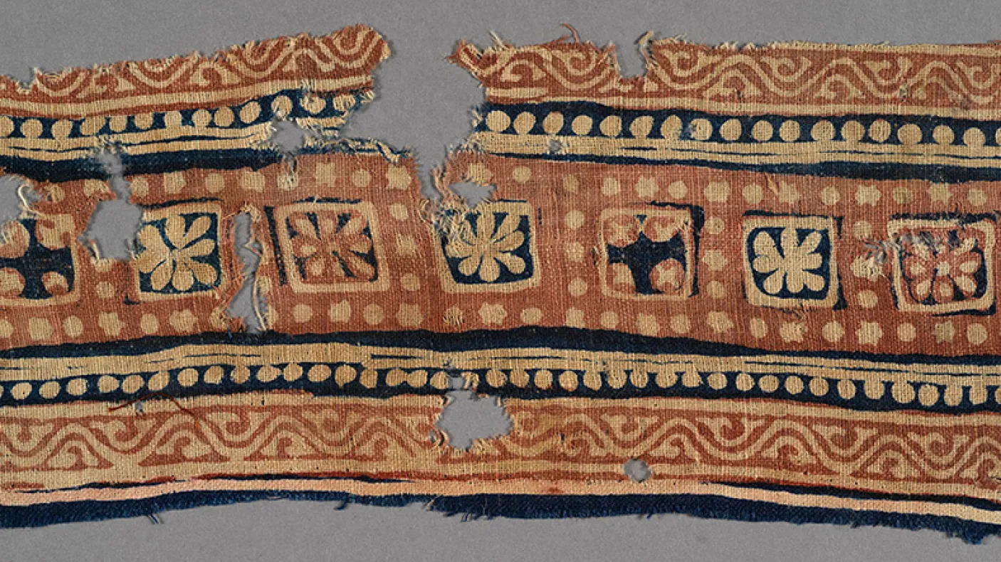 Decorative textile fragment with geometric and floral patterns in blue, beige, and red tones.