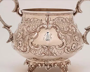 Silver ornamental bowl with two handles and intricate floral engravings surrounding a monogram with the letters "MA."