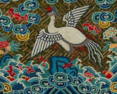 Embroidery of a white crane flying over stylized blue and green clouds with red flowers on a dark background.