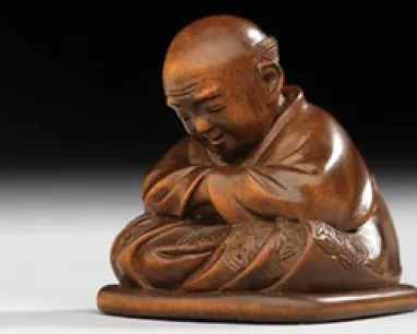 Carved wooden sculpture of a bald monk sitting cross-legged with eyes closed and arms folded.