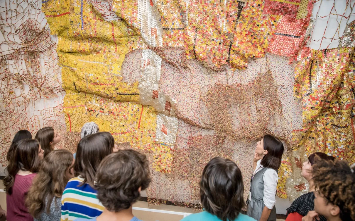 A group of people viewing a large mosaic artwork with various colors, including yellow, orange, white, and pink.