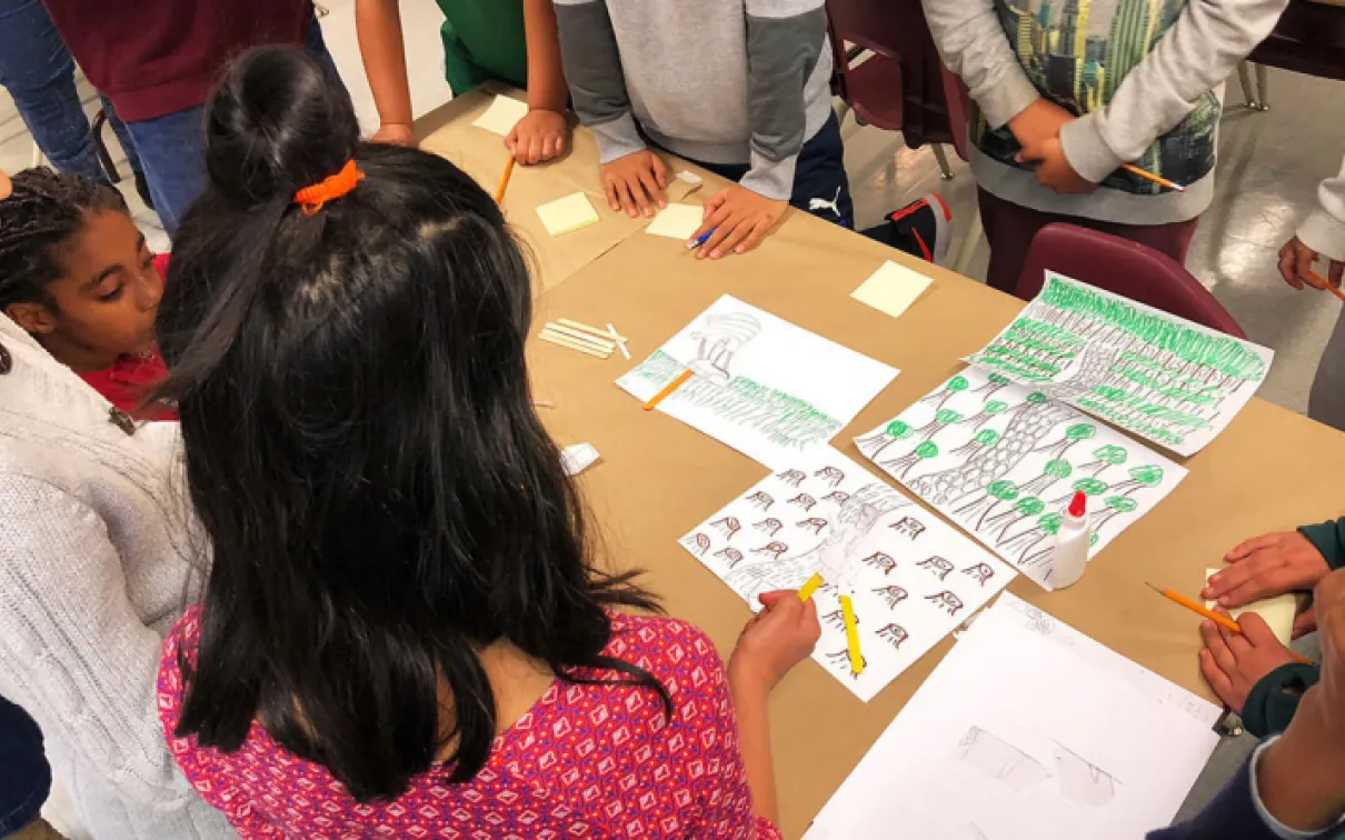 Children's hands and arms around a table with sheets of paper showing different insects and animals.