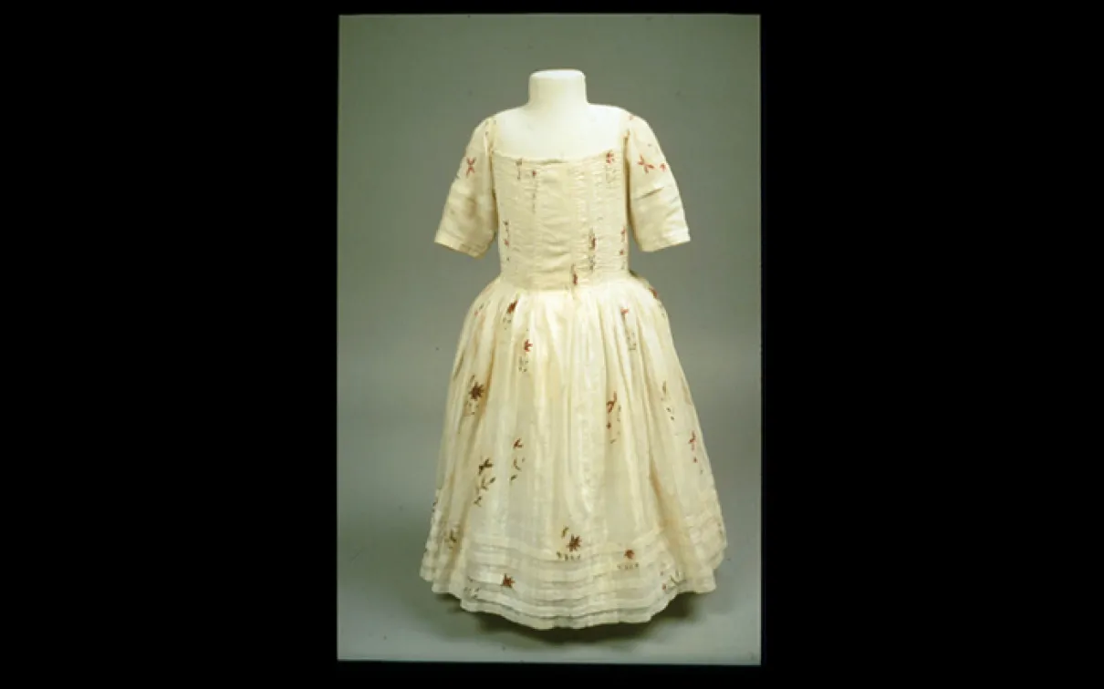 Cream-colored dress with elbow-length sleeves and a full skirt decorated with a subtle floral pattern.