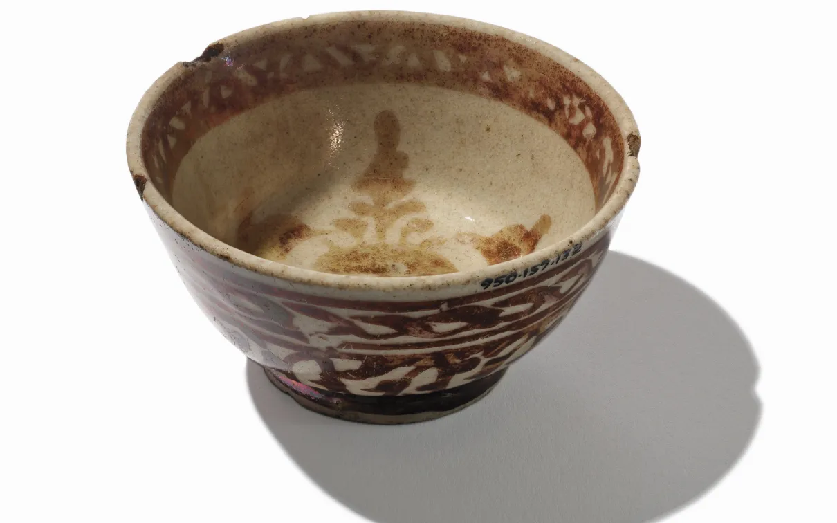 Ceramic bowl with brown floral patterns and a beige interior, casting a shadow on a white background.