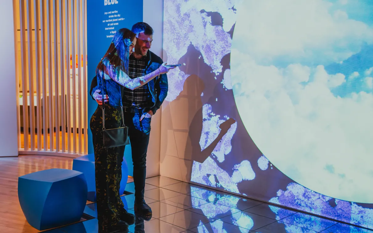 Two men interact with illuminated blue and white digital projections on a curved wall in a modern indoor space.