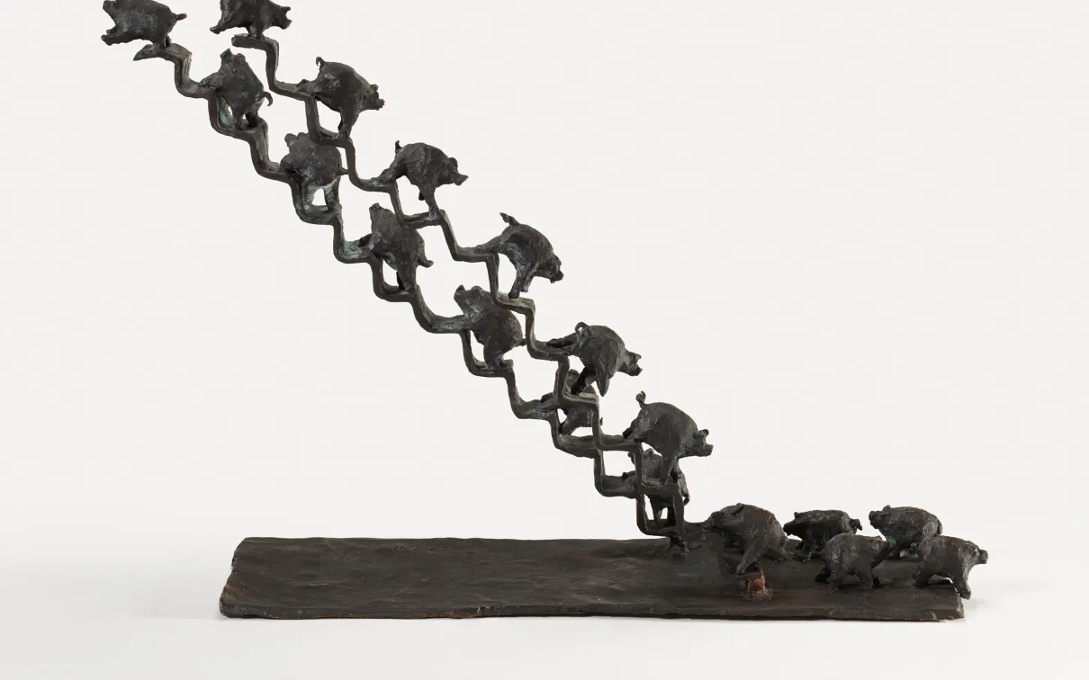 Bronze sculpture of a diagonal row of small frogs leaping upward from a flat base with three frogs on the ground.
